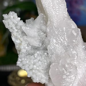 Op de afbeelding: Een cluster van witte kwartskristallen in verschillende vormen en maten. De kristallen zijn doorschijnend en hebben een licht iriserende glans.