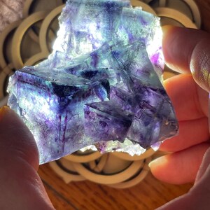 May include: A large, multi-faceted fluorite crystal with purple, green, and blue hues. The crystal is illuminated from below, highlighting its internal structure.