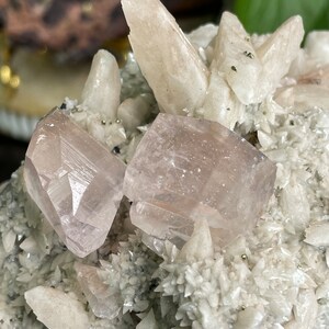 May include: A cluster of white and pink crystals with a rough, natural texture. The crystals are arranged in a variety of shapes and sizes, with some appearing to be pointed and others more rounded. The crystals are set against a dark background, which helps to highlight their natural beauty.