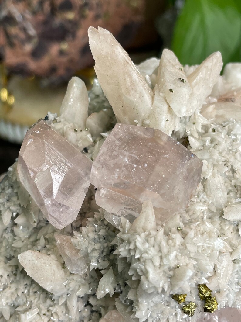 May include: A cluster of white and pink crystals with a rough, natural texture. The crystals are arranged in a variety of shapes and sizes, with some appearing to be pointed and others more rounded. The crystals are set against a dark background, which helps to highlight their natural beauty.