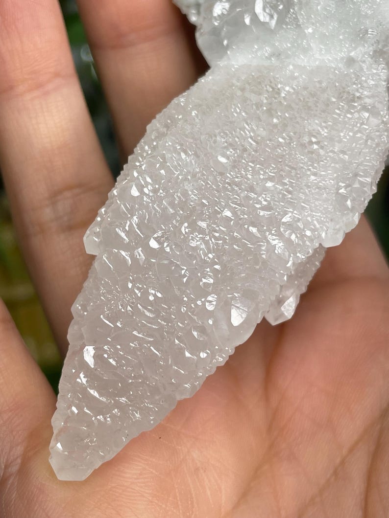 Op de afbeelding: Een witte, doorschijnende kristalkluster met een puntige, grillige vorm. De kristal heeft een ruw, getextureerd oppervlak.