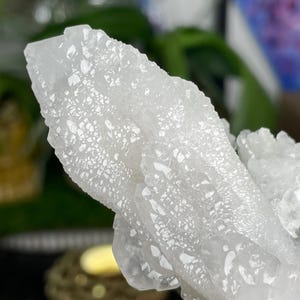 Op de afbeelding: Een cluster van witte kwartskristallen met een ruw, getextureerd oppervlak. De kristallen zijn in een natuurlijke formatie geclusterd.
