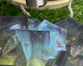 Op de afbeelding: Een cluster van groene, blauwe en paarse fluorietkristallen met vlekken van gouden pyriet. De kristallen zijn in een willekeurig patroon gerangschikt en hebben verschillende vormen en maten.