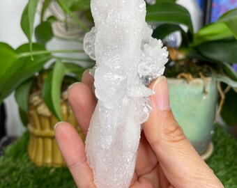 May include: A white, translucent crystal cluster with a pointed, elongated shape. The crystal has a rough, textured surface and appears to be made of many smaller crystals.
