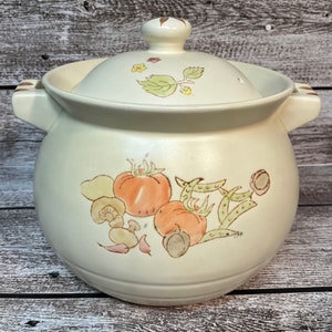 May include: A white ceramic pot with a lid, featuring a hand-painted design of tomatoes, mushrooms, and green leaves. The pot has two handles on the sides.