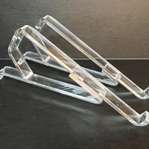 May include: Two clear acrylic stands for holding a laptop or tablet at an angle. The stands are stacked on top of each other.