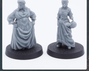May include: Two 3D printed miniature figures of women wearing long dresses and head coverings. The figure on the left is standing on a black base and the figure on the right is standing on a gray base.