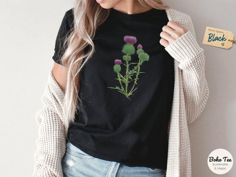 Puede incluir: Una camiseta negra con un gr&aacute;fico de una flor de cardo p&uacute;rpura. La camiseta est&aacute; hecha de materiales sostenibles y veganos. La opci&oacute;n de color es negro.