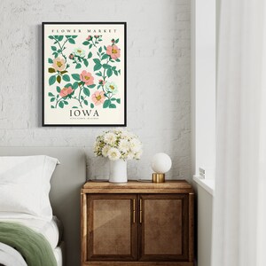 May include: A framed print with a floral design featuring pink and white flowers with green leaves. The print has the text "FLOWER MARKET" and "IOWA STATE FLOWER WILD ROSE" in black text.