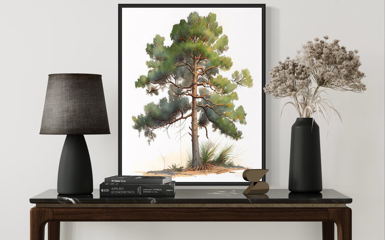 May include: A black framed print of a watercolor painting of a pine tree on a white background. The print is hanging on a white wall above a black marble topped console table. A black lamp with a gray fabric shade sits on the table, along with a black vase filled with dried flowers and a small wooden sculpture.