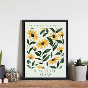 May include: A black framed print with a white background and a pattern of yellow and green flowers. The text "FLOWER MARKET" and "BLACK EYED SUSAN" is printed in black.
