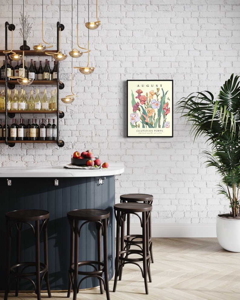May include: A framed botanical print with a white background and a floral illustration of pink, white, and orange gladiolus flowers. The print is titled "AUGUST" and "GLADIOLUS POPPY". The print is hanging on a white brick wall above a bar counter with four dark brown bar stools.