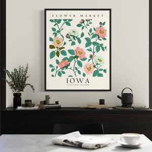 May include: A framed print with a white background and a floral illustration of pink and white flowers with green leaves. The text "FLOWER MARKET" is at the top of the print and "IOWA" is at the bottom with the text "Wild Rose" below.