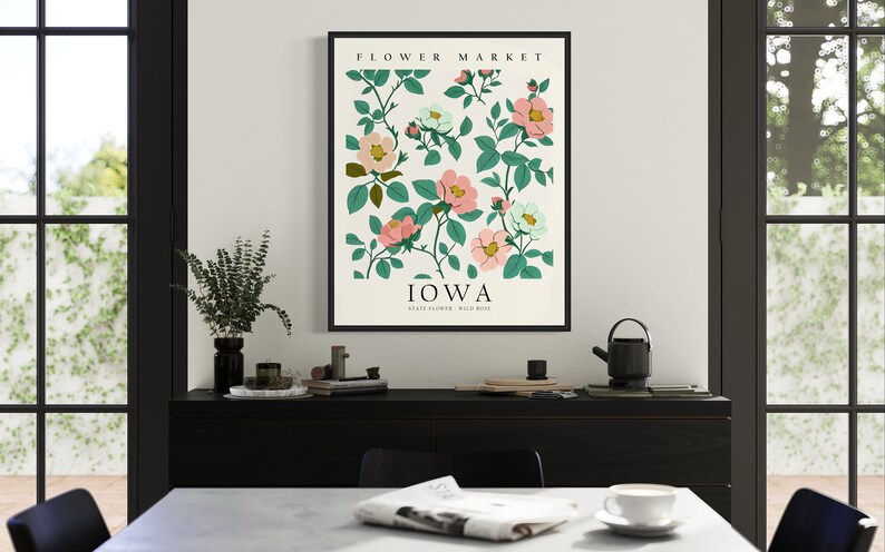 May include: A framed print with a white background and a floral illustration of pink and white flowers with green leaves. The text "FLOWER MARKET" is at the top of the print and "IOWA" is at the bottom with the text "Wild Rose" below.
