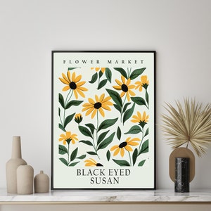 May include: A framed print with a white background and a pattern of yellow black-eyed Susan flowers with green leaves. The print has the text "FLOWER MARKET" at the top and "BLACK EYED SUSAN" at the bottom.