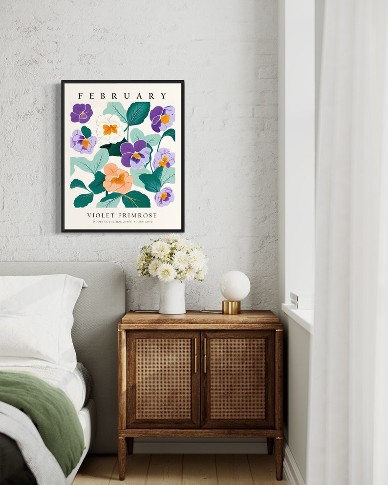 Puede incluir: Una impresi&oacute;n enmarcada con una ilustraci&oacute;n floral de flores moradas, blancas y naranjas con hojas verdes. El texto "FEBRERO" y "PRIMULA VIOLETA" est&aacute; impreso debajo de la ilustraci&oacute;n.