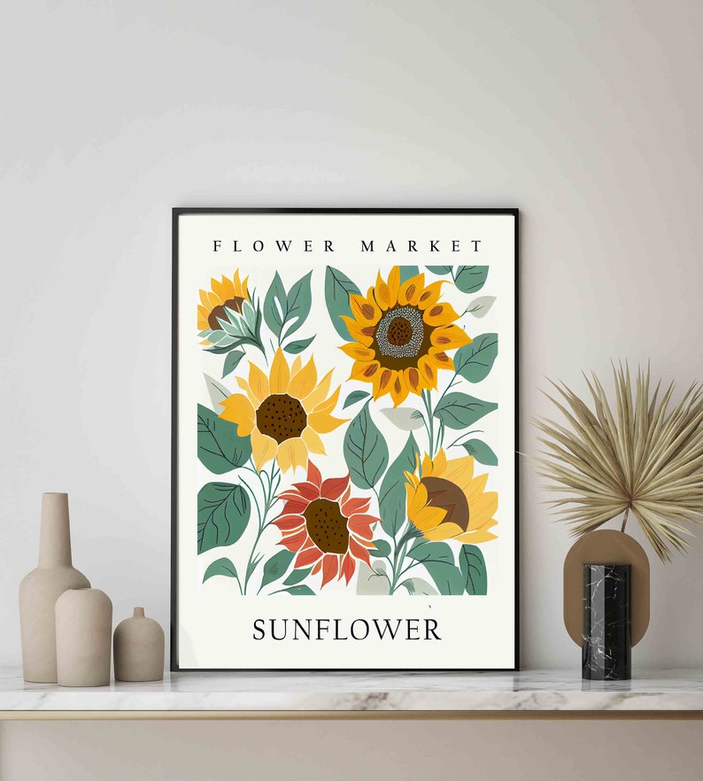 May include: A black framed print with a white background featuring a floral illustration of sunflowers in shades of yellow, orange, and green. The text "FLOWER MARKET" is at the top of the print and "SUNFLOWER" is at the bottom.