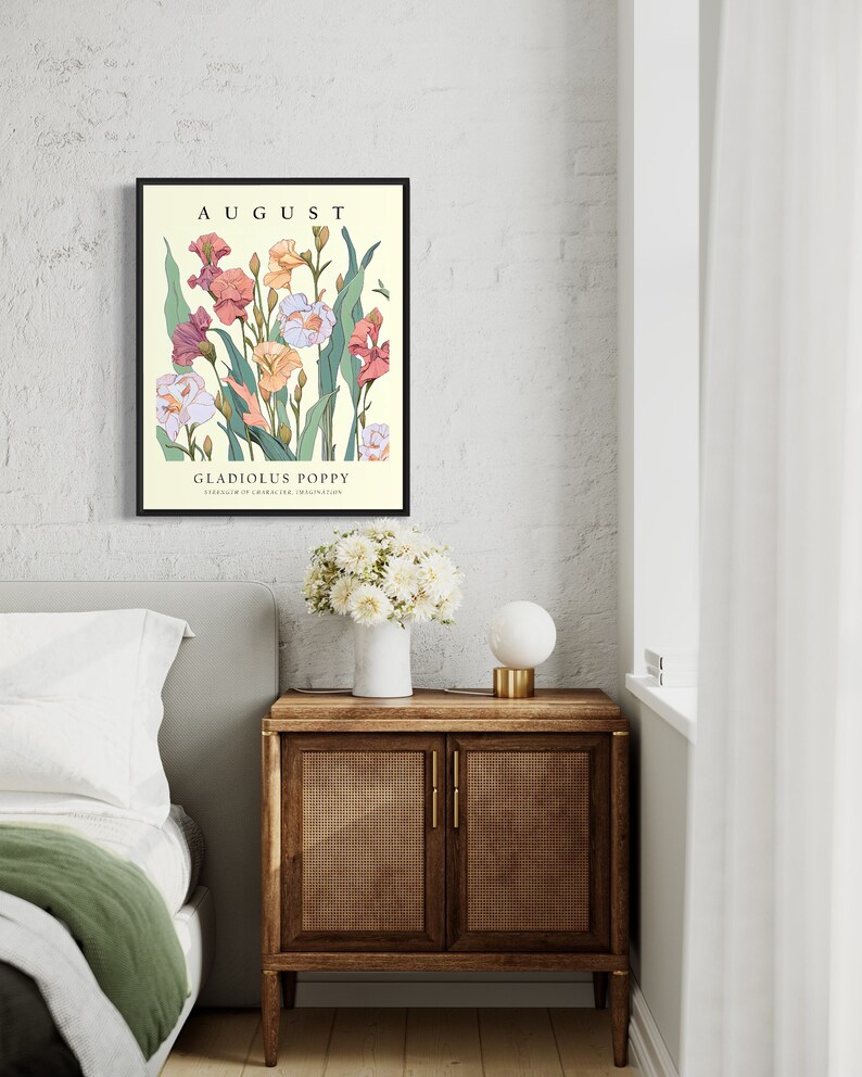 May include: A framed print with a floral illustration of pink, white, and yellow flowers with green leaves. The text "AUGUST" is at the top of the print and "GLADIOLUS POPPY" is at the bottom. The print is hanging on a white brick wall.
