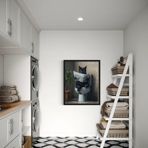 May include: A black cat sitting on a toilet reading a newspaper in a framed picture. The picture is hanging on a white wall in a laundry room with a white tiled floor, a white shelf with baskets, and a washer and dryer.