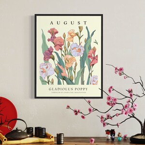 May include: A framed print with a vintage aesthetic featuring a bouquet of pink, white, and orange gladiolus flowers with green leaves. The print has the text "AUGUST" at the top and "GLADIOLUS POPPY" with the text "STRENGTH OF CHARACTER, IMAGINATION" below the flower illustration.
