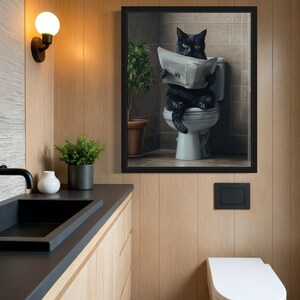 May include: A black cat sitting on a toilet reading a newspaper in a framed picture. The picture is hanging on a wood panel wall in a bathroom.