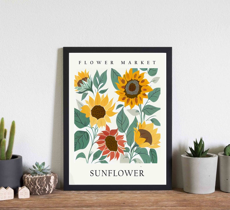 May include: A black framed print with a white background featuring a floral illustration of sunflowers in various shades of yellow, orange, and red. The text "FLOWER MARKET" and "SUNFLOWER" are printed in black at the top and bottom of the print.