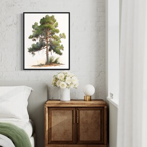 May include: A framed watercolor painting of a green pine tree with a brown trunk against a white background. The painting is hanging on a white brick wall above a wooden nightstand with a white vase of white flowers and a white lamp.