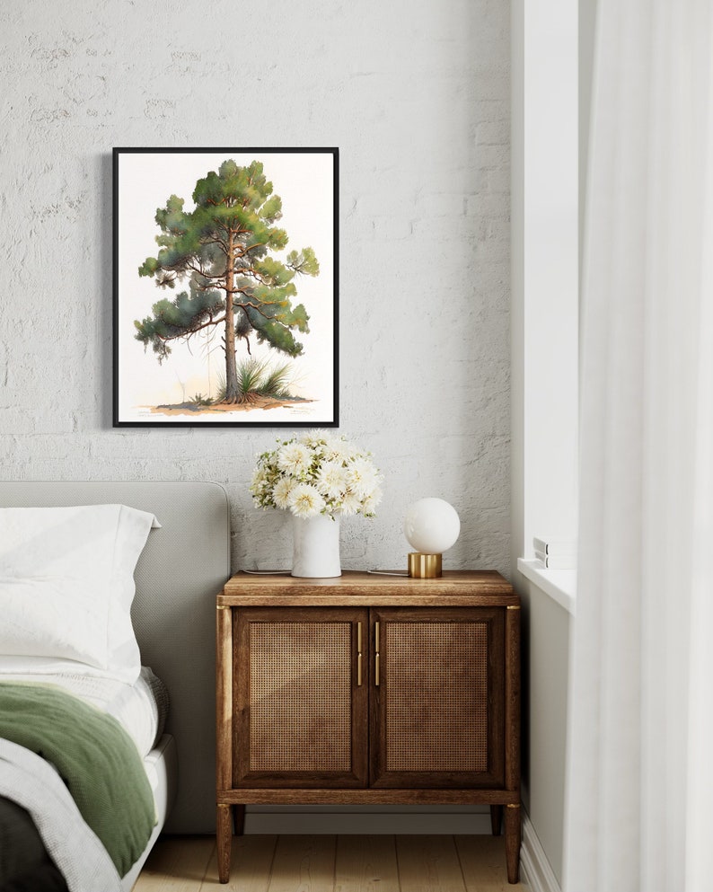 May include: A framed watercolor painting of a green pine tree with a brown trunk against a white background. The painting is hanging on a white brick wall above a wooden nightstand with a white vase of white flowers and a white lamp.