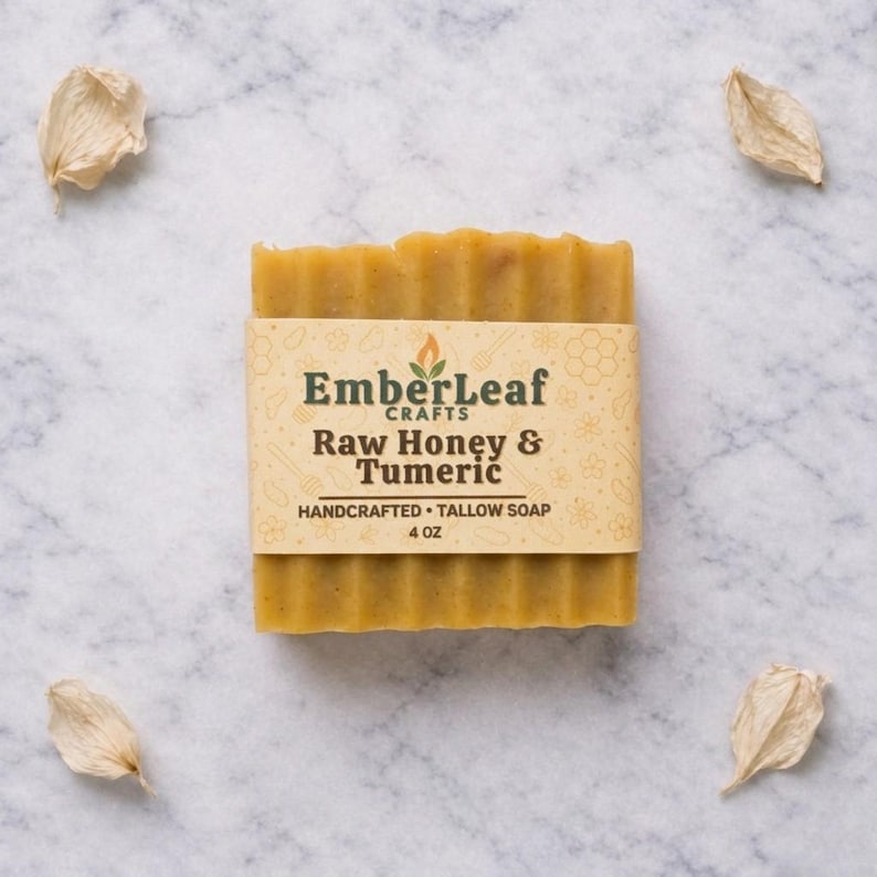 May include: A rectangular bar of handcrafted tallow soap with the label "EmberLeaf Crafts Raw Honey & Tumeric". The soap is a light yellow color and is 4 oz. Four dried petals are scattered around the soap on a white marble surface.