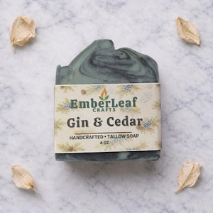 May include: A handcrafted, 4 oz. bar of soap with a marbled teal and black design. The soap is wrapped with a label that reads "EmberLeaf Crafts Gin & Cedar Handcrafted Tallow Soap."