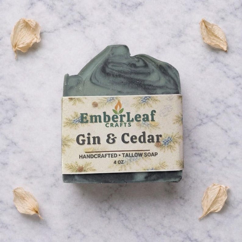 May include: A handcrafted, 4 oz. bar of soap with a marbled teal and black design. The soap is wrapped with a label that reads "EmberLeaf Crafts Gin & Cedar Handcrafted Tallow Soap."