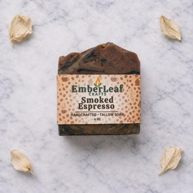 May include: A handcrafted bar of Smoked Espresso tallow soap, 4 oz, with a brown and black marbled design. The soap is wrapped with a label featuring the EmberLeaf Crafts logo and coffee bean illustrations. Four dried petals are scattered around the soap on a marble surface.
