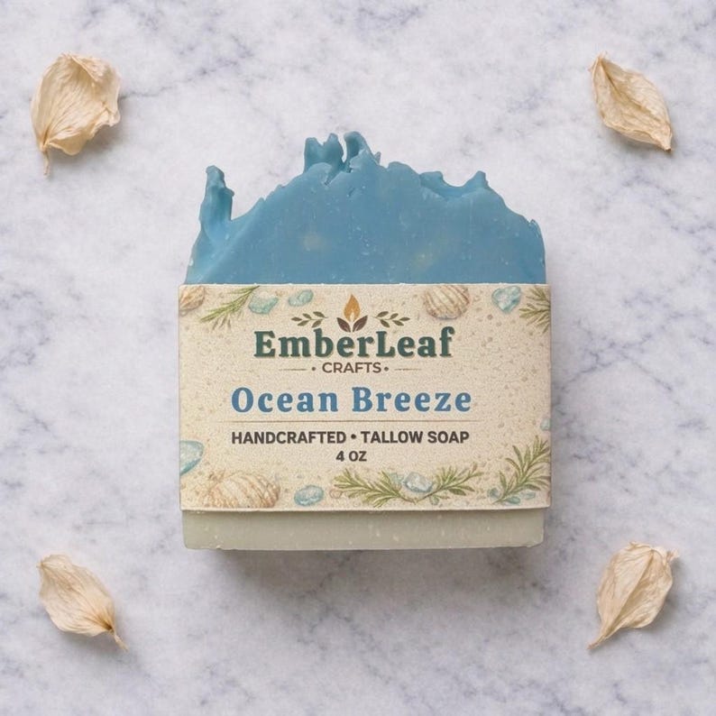 May include: A handcrafted Ocean Breeze tallow soap bar from EmberLeaf Crafts. The soap features a light blue top with a textured design, and a label with the product name and weight, 4 oz. The label is decorated with seashells and sprigs.