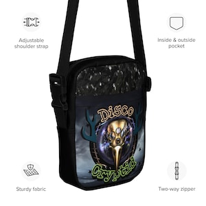 Può includere: Una borsa a tracolla nera con spallaccio regolabile, cerniera a due vie e tasca interna ed esterna. La parte anteriore presenta una grafica di un teschio d'uccello dorato con più occhi, il testo Disco Cryptid e alcune stelle.