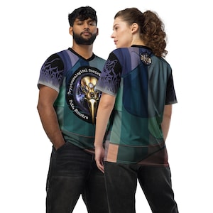 Puede incluir: Dos personas vistiendo camisas de manga corta con un estampado gráfico de una cabeza de pájaro con engranajes y el texto "Cryptozoological Society Fitey Monstra". La camisa de la izquierda es azul, verde y negra. La camisa de la derecha es azul, verde y marrón.