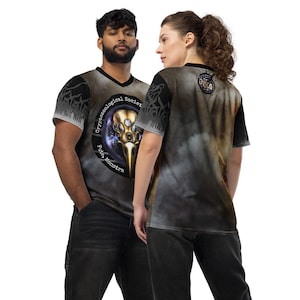 Puede incluir: Dos personas llevan puestas camisas negras de manga corta con un estampado gráfico. La camisa de la izquierda tiene un diseño negro y dorado con el texto "Cryptozoological Society, Filia Monstra". La camisa de la derecha tiene un diseño negro y dorado con un gráfico de bola de discoteca.