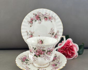May include: A white teacup and saucer set with a floral pattern of pink and purple roses. The set is made of fine bone china and has a gold trim.