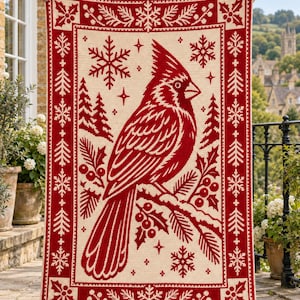 Könnte beinhalten: Eine rechteckige Häkeldecke mit einem großen roten Kardinalvogel auf einem Ast. Das Design zeigt rote und cremefarbene Muster aus Schneeflocken, Tannenbäumen und Stechpalmenbeeren. Der Rand ist dunkelrot und mit einem Stechpalmenmotiv verziert.