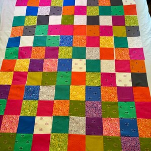May include: A patchwork quilt top composed of numerous square fabric pieces in a wide variety of colors including orange, pink, green, blue, yellow, and white, featuring various patterns and a plush green frog toy positioned at the top edge.