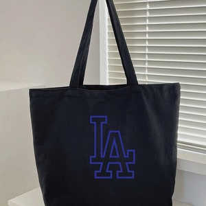 Pode incluir: Sacola de lona preta com um logotipo "LA" azul.