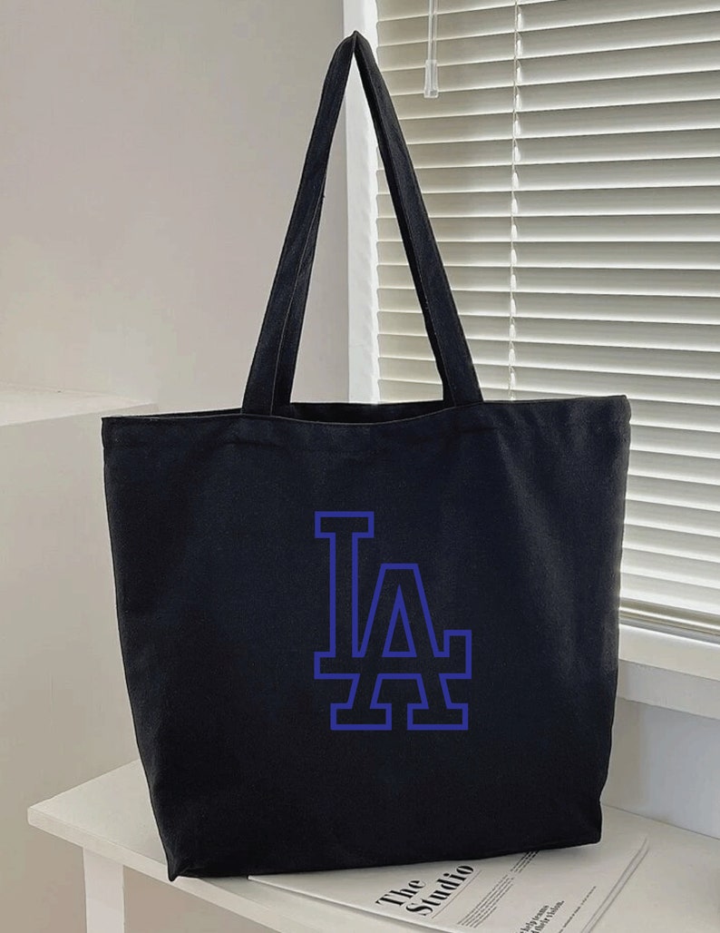 Pode incluir: Sacola de lona preta com um logotipo "LA" azul.