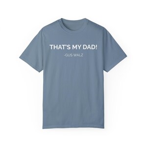 Puede incluir: Una camiseta azul claro con el texto "THAT'S MY DAD! -GUS WALZ" impreso en blanco.