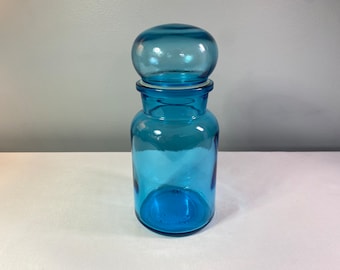 以下が含まれることがあります： 丸い蓋が付いた青いガラスの瓶。瓶は透明で、表面が滑らかです。