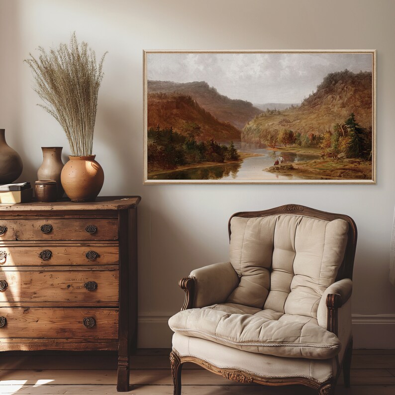 K&ouml;nnte beinhalten: Ein gerahmtes Landschaftsgem&auml;lde, das einen Fluss zeigt, der sich durch ein Tal mit &uuml;ppigen gr&uuml;nen B&auml;umen und sanften H&uuml;geln schl&auml;ngelt. Das Gem&auml;lde ist vor einem bew&ouml;lkten Himmel mit einer weichen, ged&auml;mpften Farbpalette platziert.