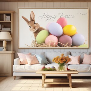 Puede incluir: Una impresi&oacute;n enmarcada con un conejo marr&oacute;n asom&aacute;ndose de un nido de heno con huevos de Pascua coloridos. La impresi&oacute;n dice "Happy Easter" en una fuente cursiva.
