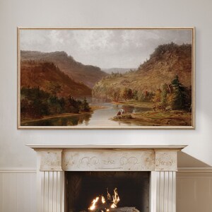 K&ouml;nnte beinhalten: Ein gerahmtes Landschaftsbild, das einen Fluss zeigt, der sich durch ein Tal mit sanften H&uuml;geln und B&auml;umen in Herbstfarben schl&auml;ngelt. Das Bild ist in einem hellen Holzrahmen gefasst und h&auml;ngt an einer wei&szlig;en Wand.