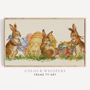 May include: A watercolour painting featuring three brown rabbits, Easter eggs, and a basket. The rabbits are in a grassy field with colourful eggs in the background. The text "COLOUR WHISPERS FRAME TV ART" is at the bottom.
