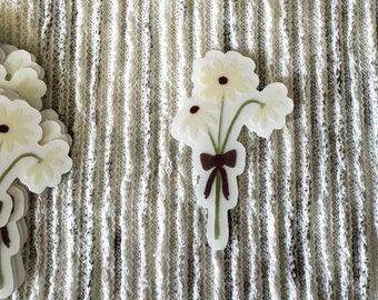 May include: A bouquet of white daisies with brown ribbon tied at the stems. The daisies are on a white and gray striped background.