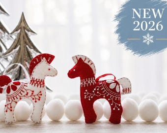 May include: Two felt horse ornaments, one white with red embroidery and one red with white embroidery, featuring intricate floral patterns and a white ribbon loop for hanging. A blue circular graphic displays the text NEW 2026 with a snowflake icon.