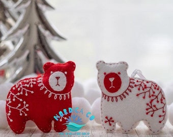 May include: Two felt Christmas ornaments shaped like bears. One bear is red with white embroidery and the other is white with red embroidery. Both bears have a red nose and eyes. The ornaments are hanging from a white string.